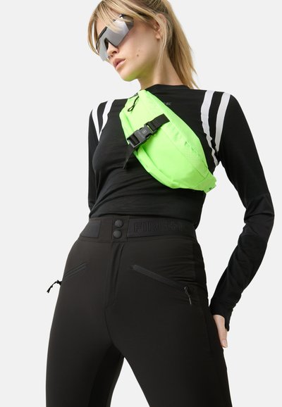 Neon green crossbody bag, black long-sleeve top with stripes, and high-waisted black pants with zippered pockets and button closure.
