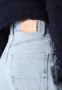 Světle modré džíny s vysokým pasem, které mají koženou nášivku značky "ONLY" na zadní straně a klasický design s pěti kapsami.