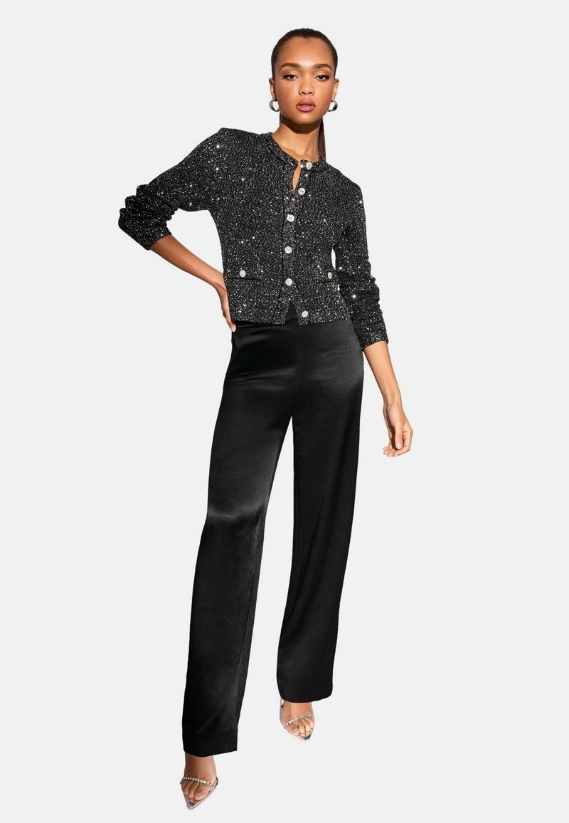 Svart paljett cardigan med rund halsringning och knappstängning, kombinerad med högmidjade svarta satinklänningar och sandaler med klara klackar.