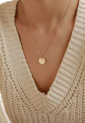 Collier en or avec un pendentif rond, suspendu à une chaîne délicate. Porté sur un pull en tricot texturé de couleur crème avec un décolleté en V.