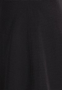 Czarna tkanina o fakturowanym, kratkowanym wzorze. Materiał wydaje się miękki i lekko układa się, tworząc gładką powierzchnię z głębią.