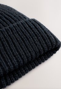 Crna rebrasta pletena kapa od mekanog vunenog materijala; s preklopljenim rubom i teksturiranim izgledom, pogodna za hladno vrijeme.