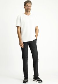 Witte T-shirt met korte mouwen en ronde hals, gecombineerd met strakke zwarte broek en zwarte sportschoenen. Eenvoudig, modern ontwerp.