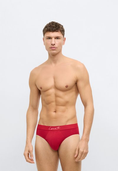Piros pamut alsónadrág rugalmas derékpánttal, amelyen világos rózsaszín "Love" felirat található. A szövet sima tapintású.