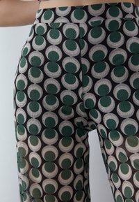 Patterned wide-leg trousers featuring green and cream circular designs on a black background. Made from a lightweight, textured fabric.