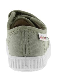 Bottine en toile verte sans lacets avec semelle en caoutchouc blanche. Présente un design cousu, un bout arrondi et une étiquette de logo colorée sur le talon.