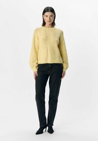 Yellow knitted sweater with textured diamond pattern, balloon sleeves, paired with black straight-leg jeans and black pointed-toe heels.