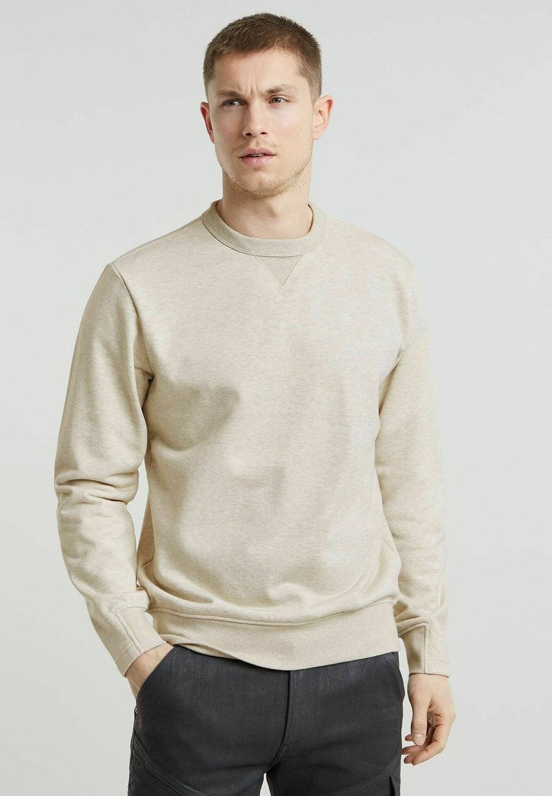 Sweatshirt beige con scollatura a girocollo, maniche lunghe e tessuto testurizzato. Presenta polsini a coste e un logo discreto sul petto.