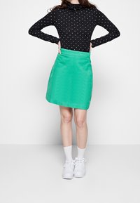 Svart långärmad topp med vita prickar och en grön A-linjeformad kjol, kombinerad med vita sneakers och ankelstrumpor. Slät tygkvalitet.