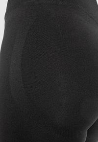 Zwarte leggings met een soepele, rekbare textuur. Belangrijk ontwerpkenmerk: naden langs de achterkant voor vormgeving. Elastische tailleband.