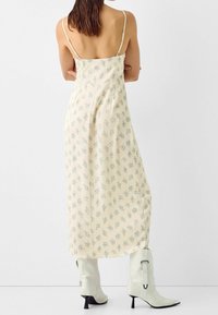 Maxi šaty v světle žluté barvě s květinovým potiskem v modré a zelené barvě. Vyrobené z lehké látky, mají nastavitelné tenké ramínka a boční rozparek.