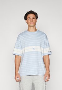 Lysblå stribet t-shirt med hvide vandrette striber, rund halsudskæring og logo detalje på brystet og ærmet, lavet af blødt bomuldsstof.
