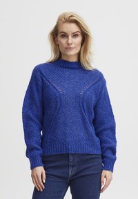 Blå stickad tröja med hög halsringning, texturerat mönster och utskärningar framtill. Ribbad mudd och kant.