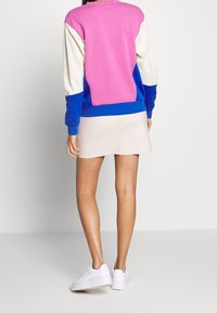 Colorful sweatshirt with pink, blue, and cream sections; features a relaxed fit and ribbed cuffs. Worn with a light skirt and white sneakers.
