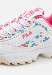 Baskets blanches de sport avec des accents de motifs multicolores en bleu et rouge, présentant une tige en cuir texturé et une semelle en caoutchouc avec des rainures.