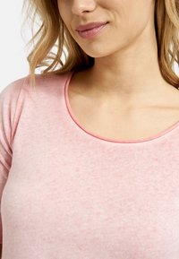 Helles Rosa, weiches Baumwolloberteil mit weitem Rundhalsausschnitt und kurzen Ärmeln. Der Stoff hat eine subtile Textur und ein leicht meliertes Muster.