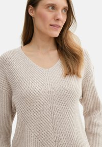 Stickad beige tröja med V-hals, med ett strukturerat, diagonalt mönster. Bekväm passform med långa ärmar, tillverkad av mjukt material.