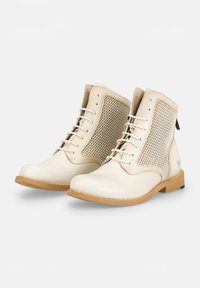 Botas de tobillo de cuero color crema con paneles laterales de malla, puntera redonda y suelas de goma marrón claro; cuentan con cordones blancos y un tacón bajo.