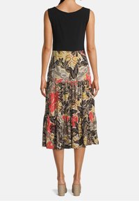 Maxiklänning med svart topp och mönstrad, flerfärgad kjol med tropiska blad och blommor, samt en lager-på-lager volangkant.