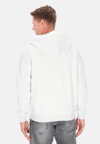 Vit hoodie av mjukt, texturerat tyg. Har en rymlig huva och muddade ärmslut. Kombinerad med grå jeans, visar en avslappnad passform.