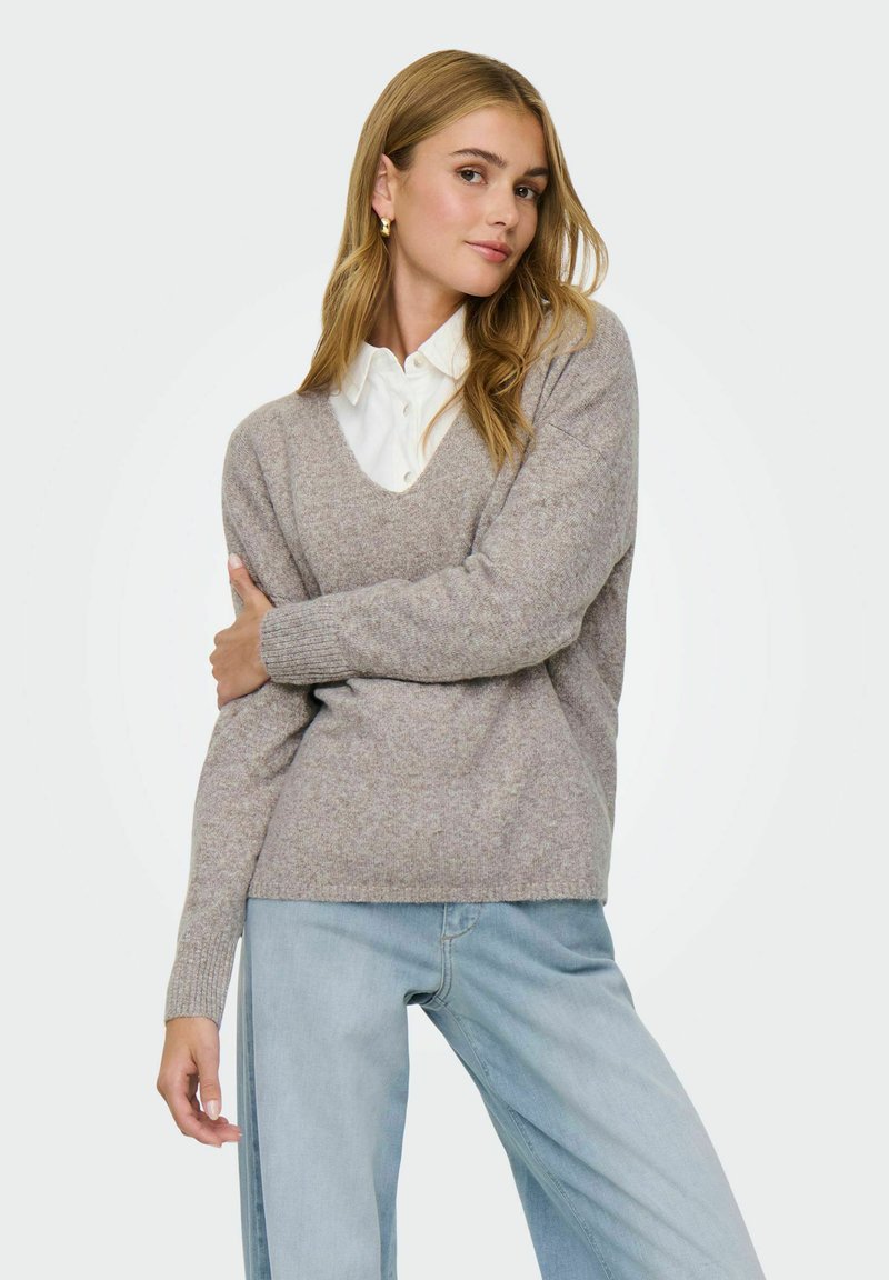 Pull en maille gris clair avec un col en V et des poignets côtelés, associé à un jean bleu clair ample. Texture douce et coupe décontractée.
