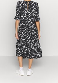 Musta kukkamekko, jossa on valkoisia kukkia, röyhelöhihat, kerroksellinen helma ja takana avaus. Yhdistetty valkoisiin lenkkareihin.