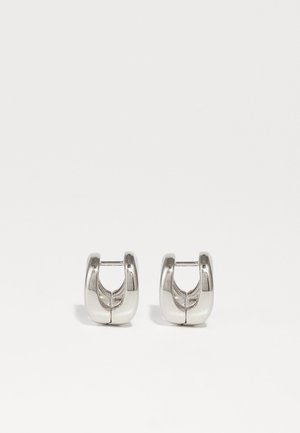 Strieborné kruhové náušnice s zaobleným tvarom, s hladkým kovovým povrchom a otvoreným dizajnom v strede, odrážajúcim svetlo.