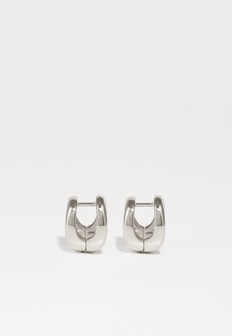 Pendientes de aro de plata con forma redondeada, presentan una superficie metálica suave y un diseño abierto en el centro, reflejando la luz.