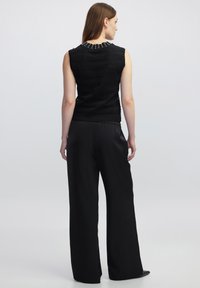 Maglietta nera senza maniche con strisce orizzontali testurizzate e perline decorative sul collo, abbinata a pantaloni neri larghi.
