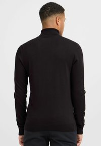 Maglione nero a maniche lunghe con colletto a imbuto realizzato in tessuto a maglia liscia, con un design aderente e polsini e orlo a costine.