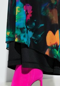 Barevné květinové šaty s průhlednou vrstvou a černou spodní vrstvou, doplněné jasně růžovými vysokými podpatky. Hladká textura a výrazný vzor.