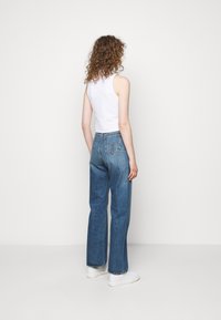 Nieco podwyższone granatowe dżinsy o szerokim kroju nogawek, z klasycznym pięciokomorowym fasonem i lekko wyblakłym odcieniem, zestawione z białą bluzką bez rękawów.