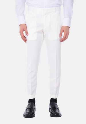 Pantaloni bianchi su misura con vestibilità slim, texture liscia, piega centrale e passanti per la cintura. Abbinati a scarpe eleganti nere e calze.