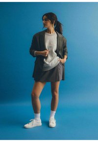 Szary sweter z napisem, czarny żakiet, szara spódnica w prążki, białe skarpetki i białe trampki na jednolitym niebieskim tle.