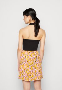 Top preto em halter com corpete ajustado; saia estampada com flores em rosa, amarelo e preto; faixa elástica na cintura; comprimento acima do joelho.