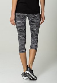 Černobílé legíny kapri s vzorem mají hladký, elastický materiál s vlnkovým designem. Spárováno s černými sportovními botami.