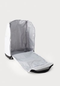 Mochila blanca con interior gris y底negro. Cuenta con un cierre de cremallera y un bolsillo lateral. El interior es espacioso con una textura lisa forrada.