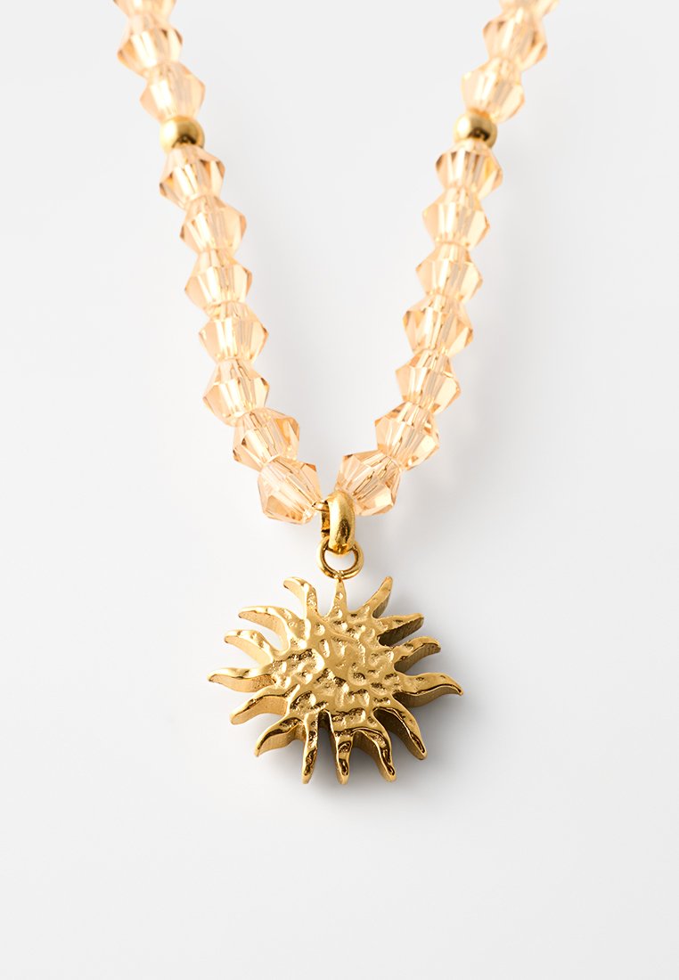 Goldenes Sonnen-Pendeln mit facettierten Pfirsichperlen und goldenen Akzenten. Der Sonnenanhänger hat ein strukturiertes, dreidimensionales Design.