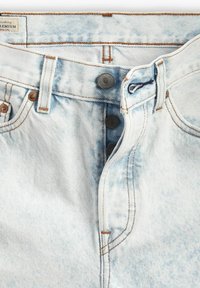 Jeans de mezclilla azul claro con cremallera, tres botones de metal y costuras en beige que contrastan a lo largo de las costuras y los bolsillos.
