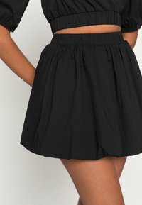 Zwarte plooienrok met een elastische tailleband. Lichtgewicht stof, boven de knie lengte, met een gladde textuur en plooien.