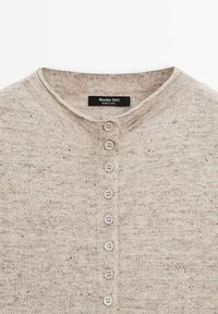 Cardigan beige en tricot avec encolure ronde et sept boutons sur le devant, étiquette Massimo Dutti, fabriqué en Chine.