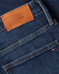 Blaue Jeans-Tasche aus Denim mit braunem Leder-Label von Tommy Hilfiger und kleinem gesticktem rot-weiß-blauen Logo am Taschenrand.