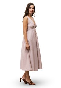 Roze linnen maxi-jurk met een diepe V-hals, knopen aan de voorkant en een vloeiende silhouette. Gecombineerd met bruine blockhak-sandalen.