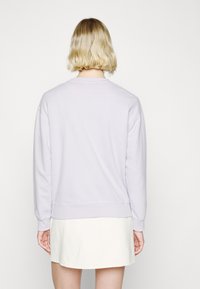 Jasnofioletowa bluza z długim rękawem, okrągłym dekoltem i ściągaczami przy rękawach. Ma gładką fakturę i wydłużony tył.