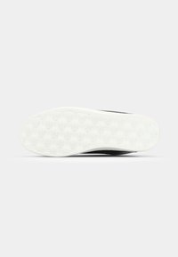 Zapatilla negra con parte superior texturizada, suela de goma y suela blanca. La suela presenta un patrón de logo repetido para mayor tracción.