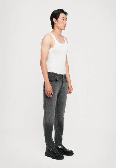 Jeans gris, débardeur blanc, chaussures noires. Les jeans ont une coupe droite et peu de détails ; le débardeur a un col rond et une texture côtelée.