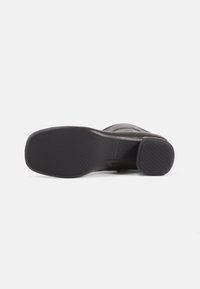 Brown leather shoe with a textured rubber sole, featuring a rounded toe and subtle design details. Sole has horizontal grooves for traction.