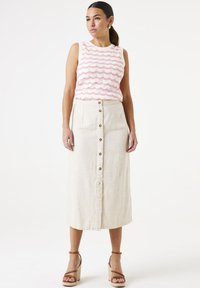 Lichtbeige linnen midi rok met knopen aan de voorkant, aangevuld met een witte top met een roze golvend patroon. Bruine sandaaltjes met bandjes op een wig.