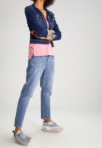 Jeansjacka med en åtsittande design, lagd över en rosa T-shirt. Avslappnade blå jeans med en lös passform och slitna detaljer. Silverfärgade sneakers.