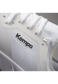 Zapatilla deportiva blanca con material de malla y sintético, que presenta acentos texturizados, cordones y un logo "Kempa" en negro.